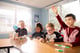 Four elementary students working together at a table in a classroom, with one student raising his hand.