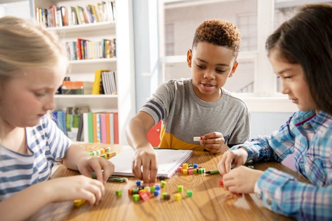 Three students at a table stack counting cubes.