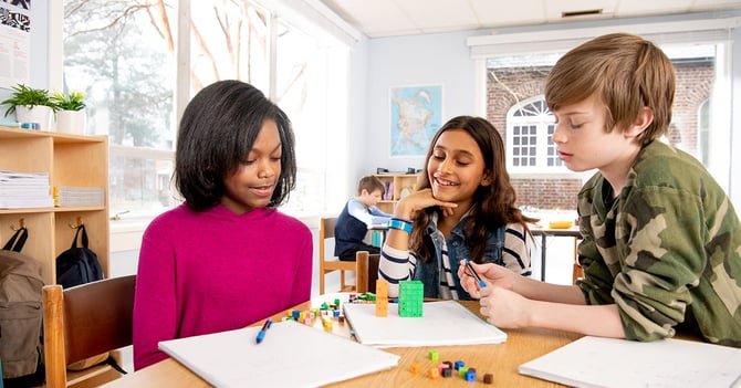 Three students sitting at a table together working with multicolored counting cubes.