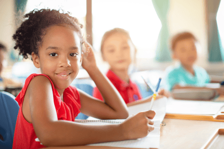 Girl writing in class with other students in the background