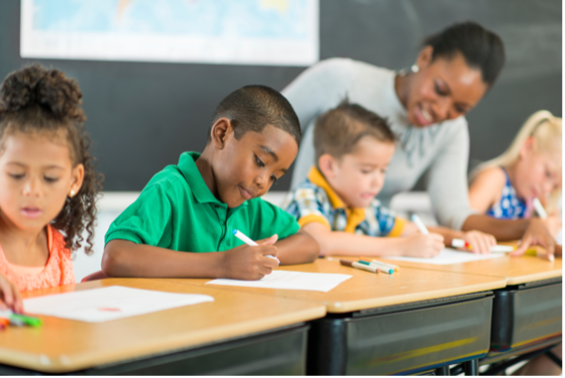 Students work at their desks while the teacher checks in with students.
